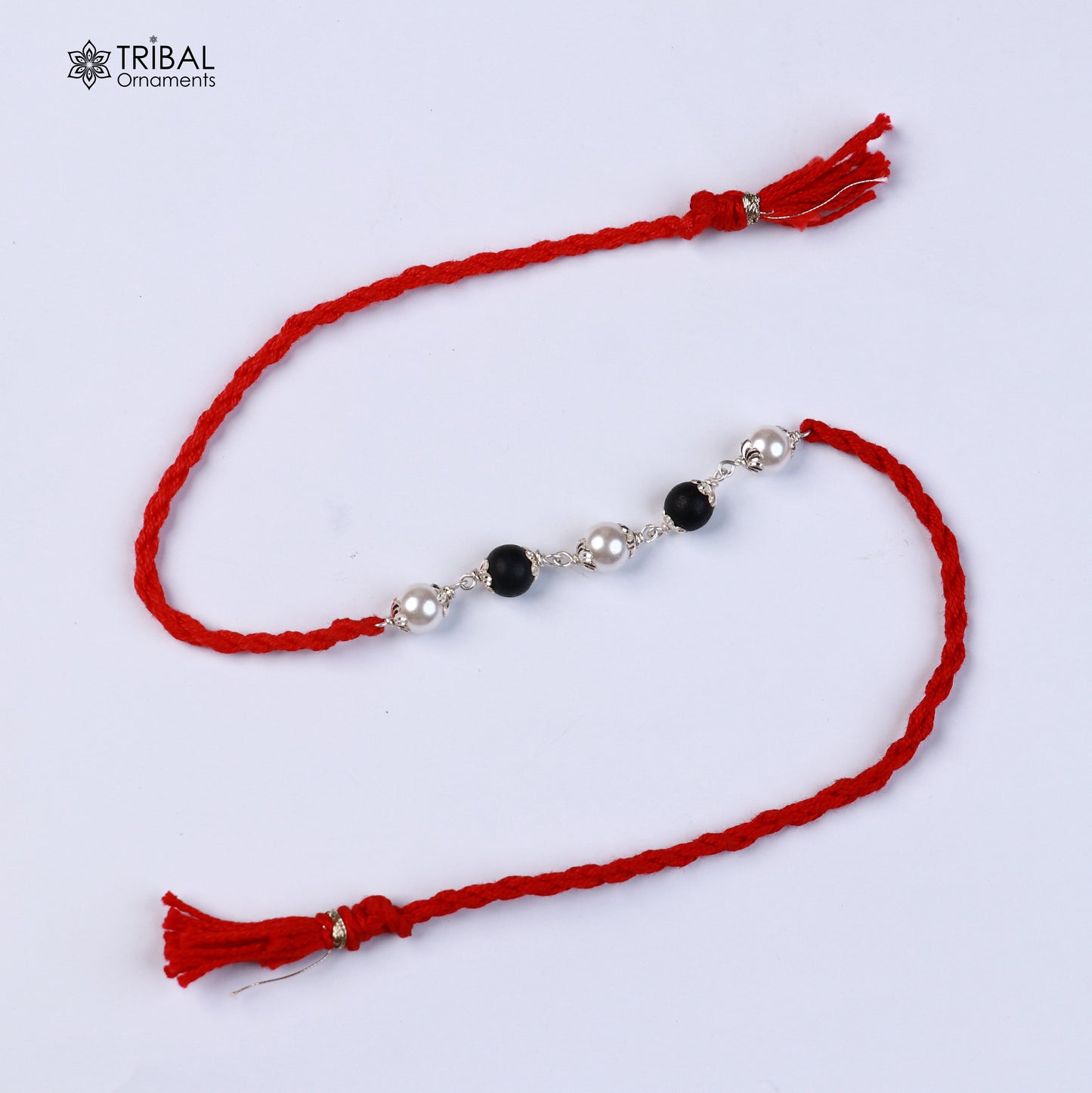 Sterling silver KARUNGALI and pearl bead Rakhi bracelet with red thread from TRIBAL ORNAMENTS, featuring intricate design.