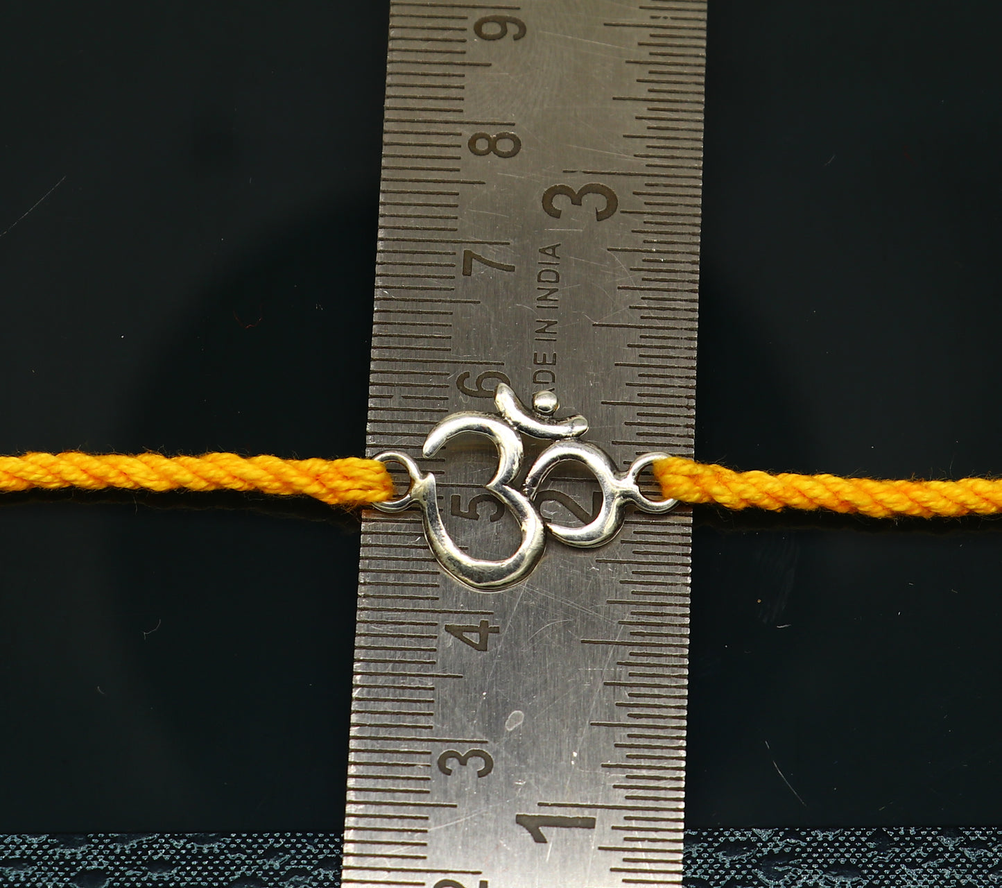 925 sterling silver OM design rakhi bracelet with yellow thread by TRIBAL ORNAMENTS, featuring custom intricate silver and thread detailing