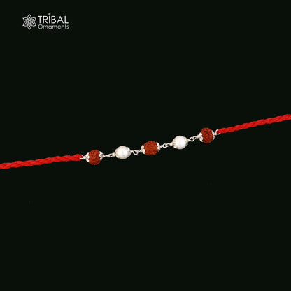 Sterling silver Rakhi bracelet with Rudraksha and pearl beads on red thread, featuring intricate tribal design.