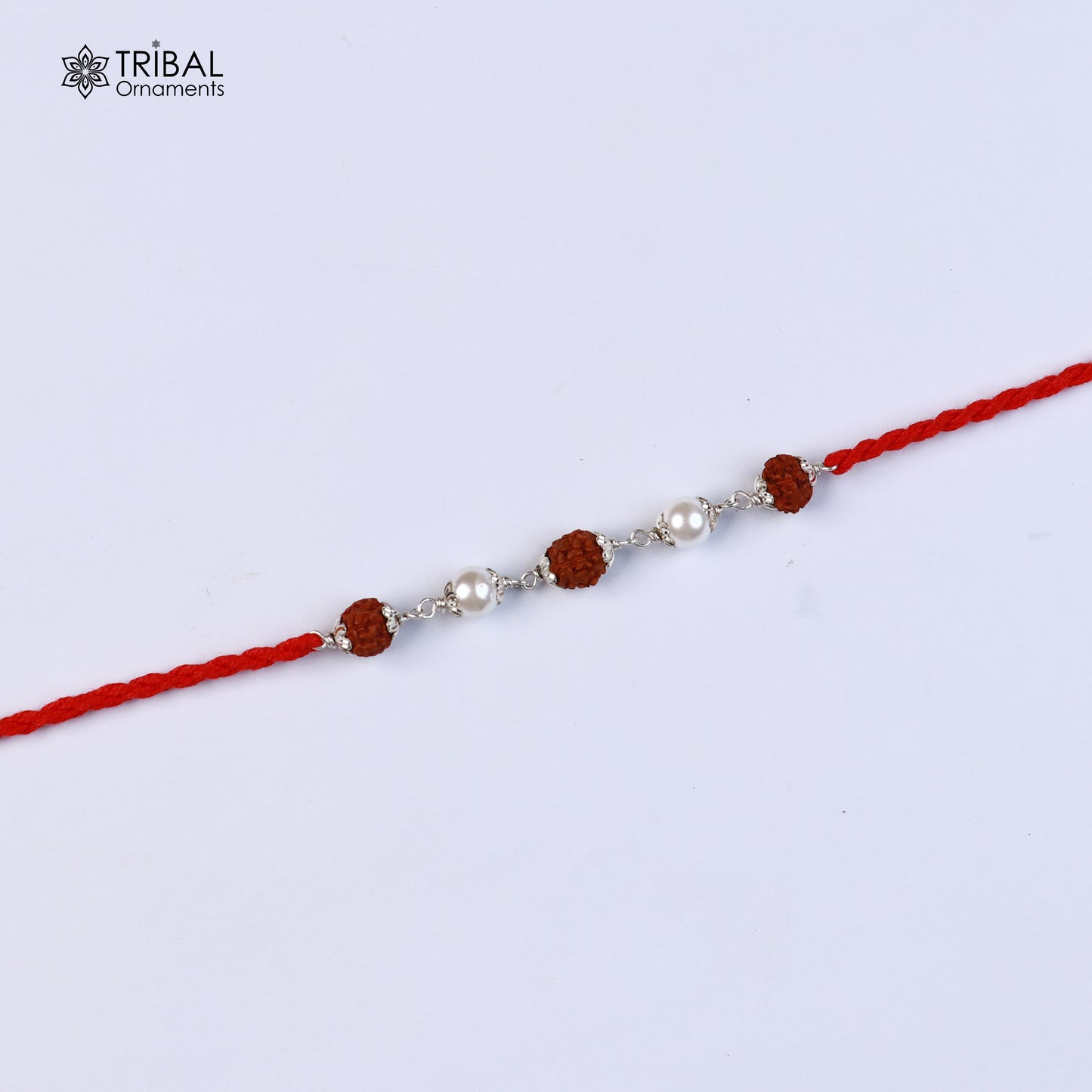 Sterling silver Rakhi bracelet with Rudraksha, pearl beads, and red thread, featuring intricate tribal ornament design.