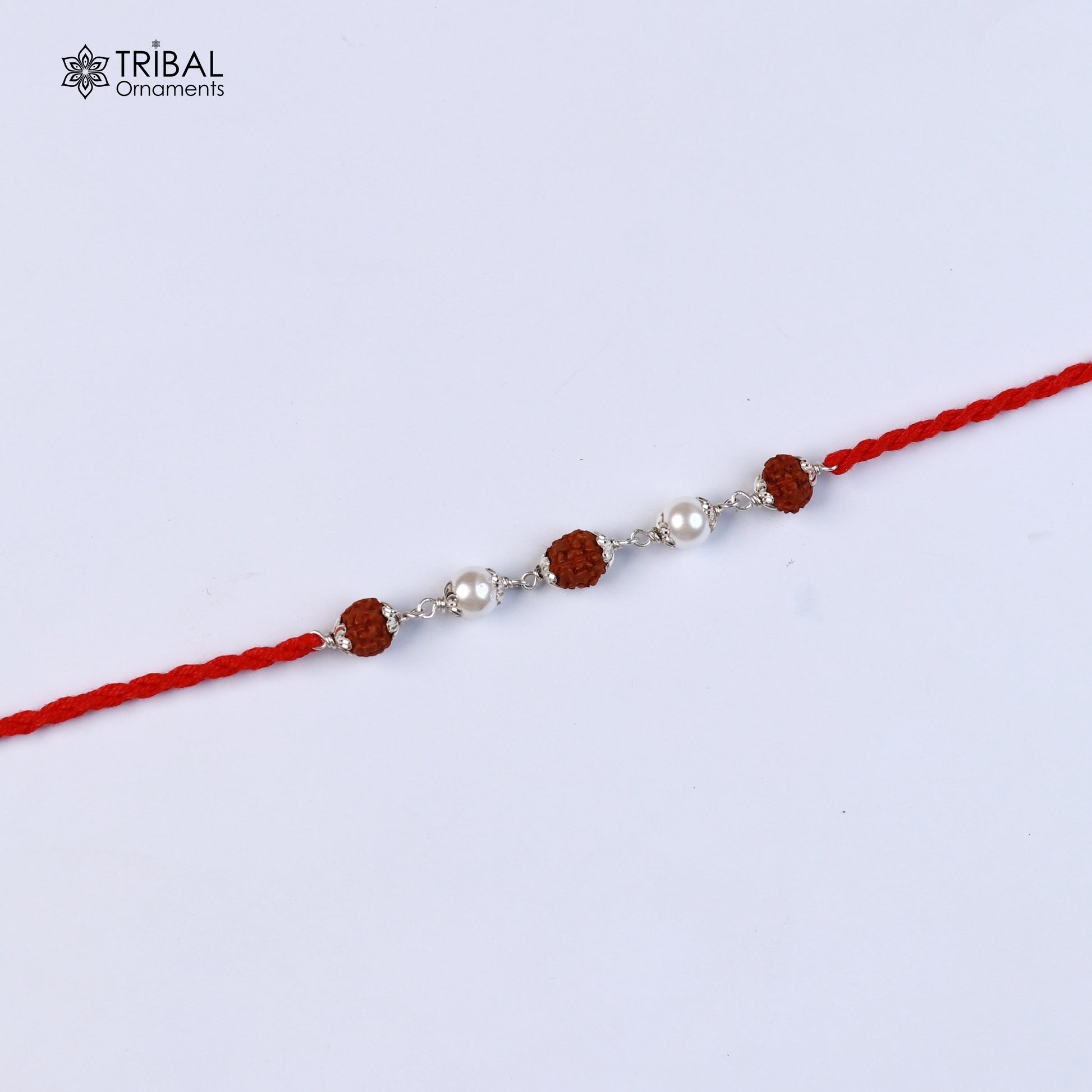 Sterling silver Rakhi bracelet with Rudraksha, pearl beads, and red thread, featuring intricate tribal ornament design.