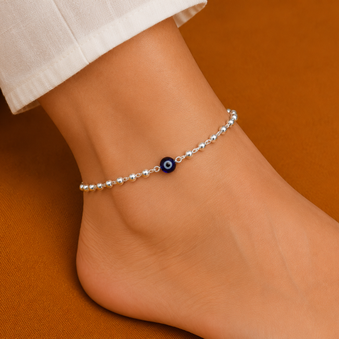 Silver evil eye anklet with blue bead and sterling silver beads for girls and kids on orange background.
