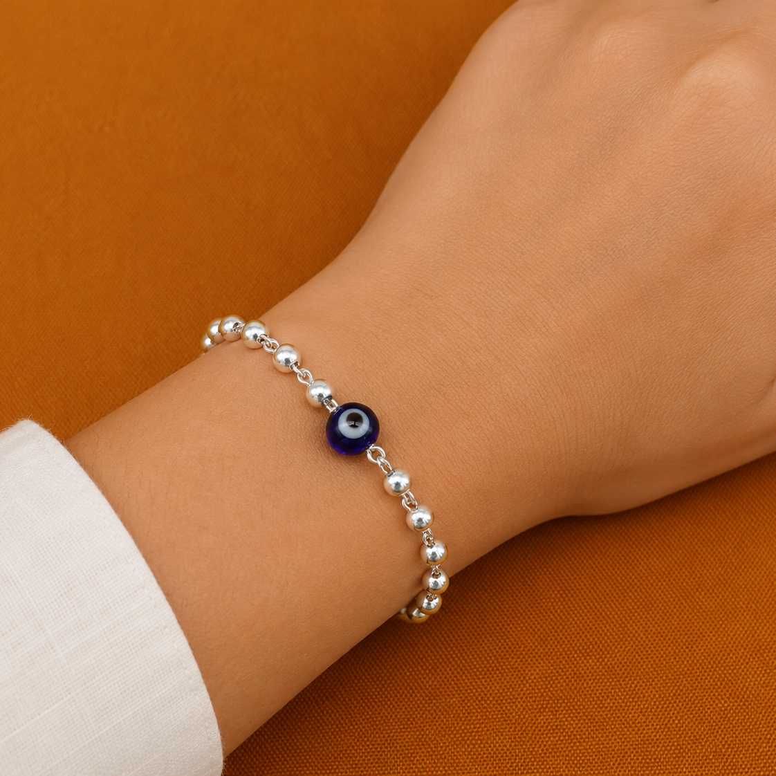 Sterling silver beaded bracelet with blue evil eye charm, designed for girls and kids, against an orange background.