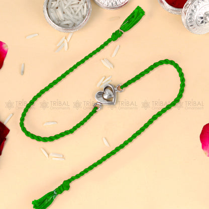 Sterling silver heart design thread rakhi bracelet by TRIBAL ORNAMENTS with red thread and silver pendant.