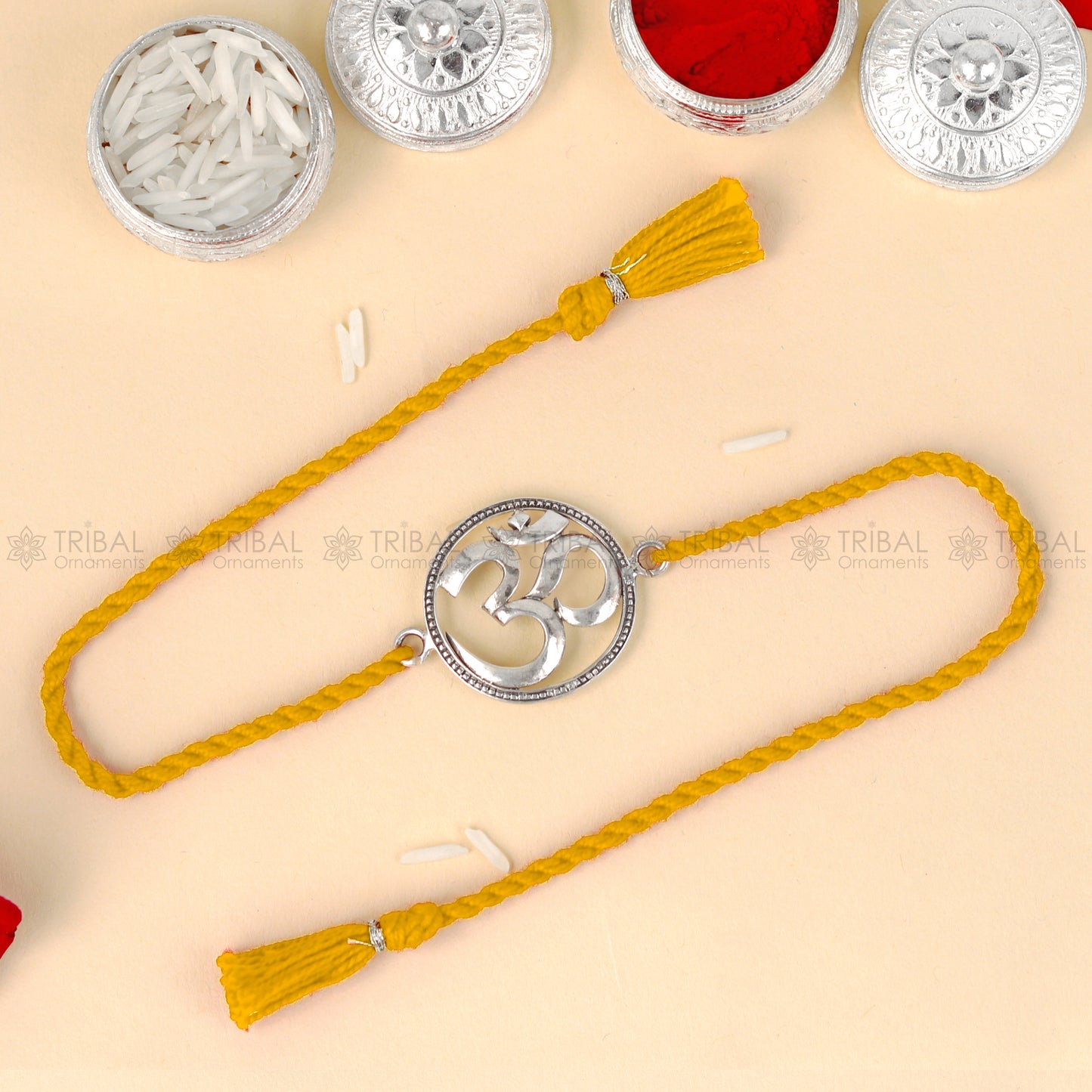 Sterling silver Om design thread rakhi bracelet with red thread from TRIBAL ORNAMENTS, featuring a detailed pendant.