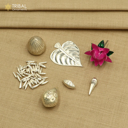 Sterling silver pooja accessories including supari, paan leaves, rice, cloves, coconut, cardamom, and flowers for worship.