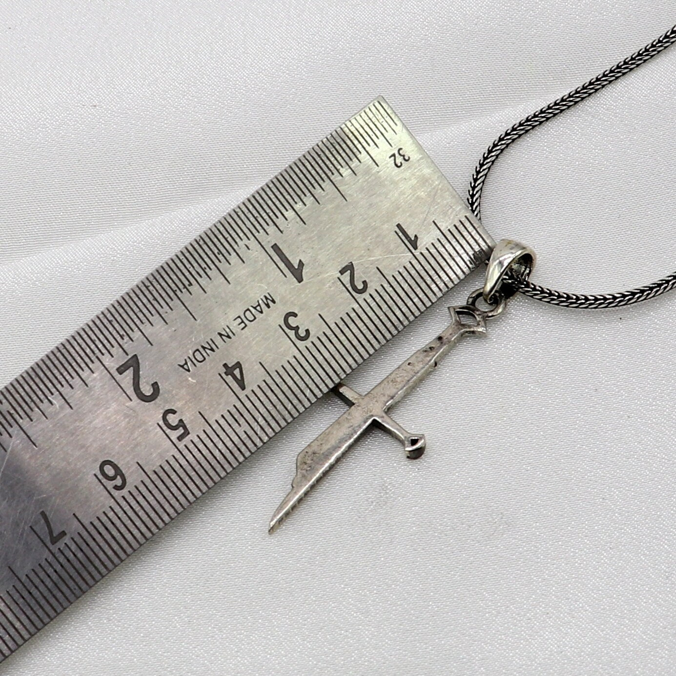 Sterling silver small sword pendant by TRIBAL ORNAMENTS, handmade unisex jewelry with white finish and intricate design.