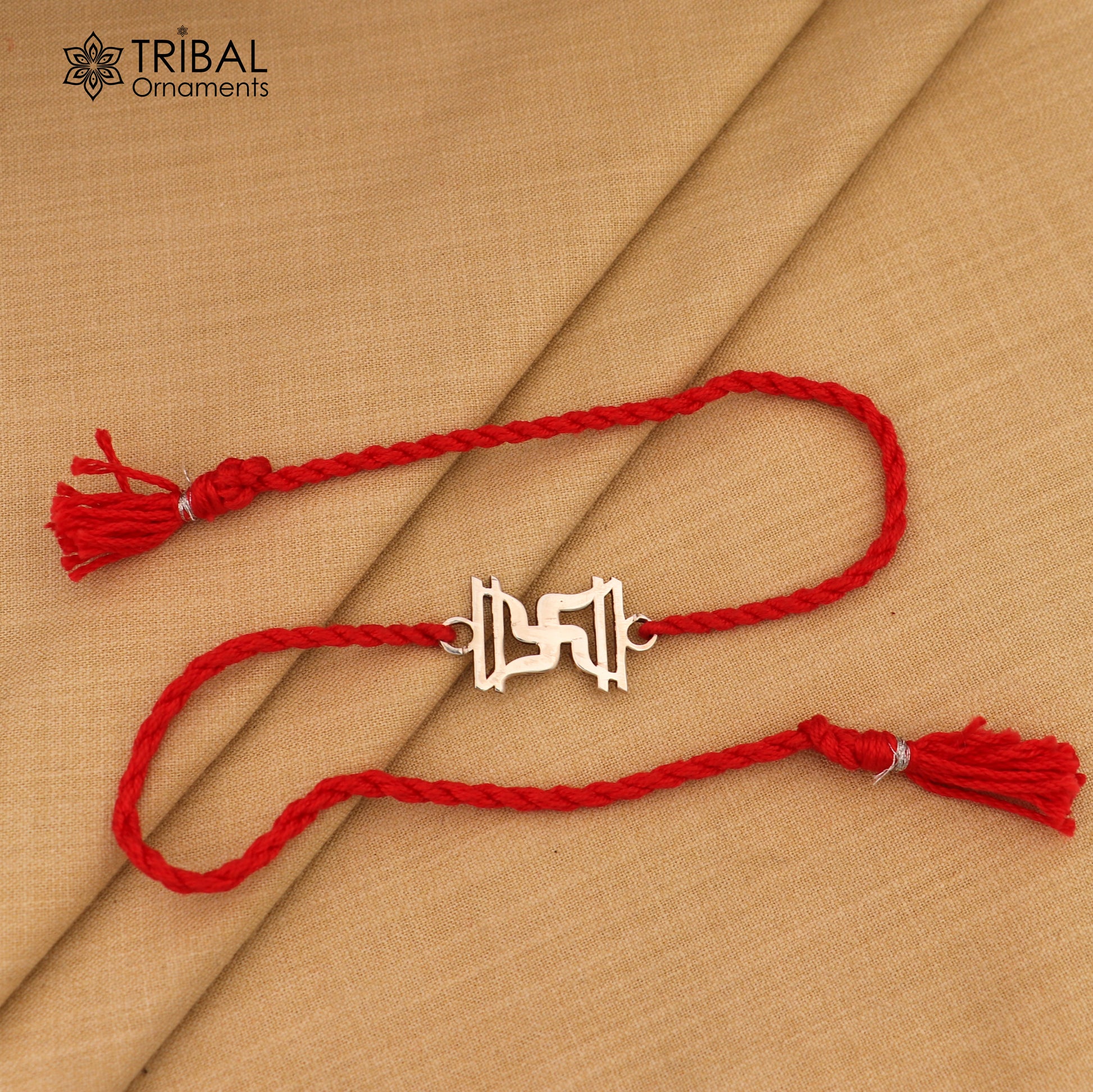 925 sterling silver Swastika rakhi with red thread from Tribal Ornaments, ideal for sibling gift, detailed silver design.