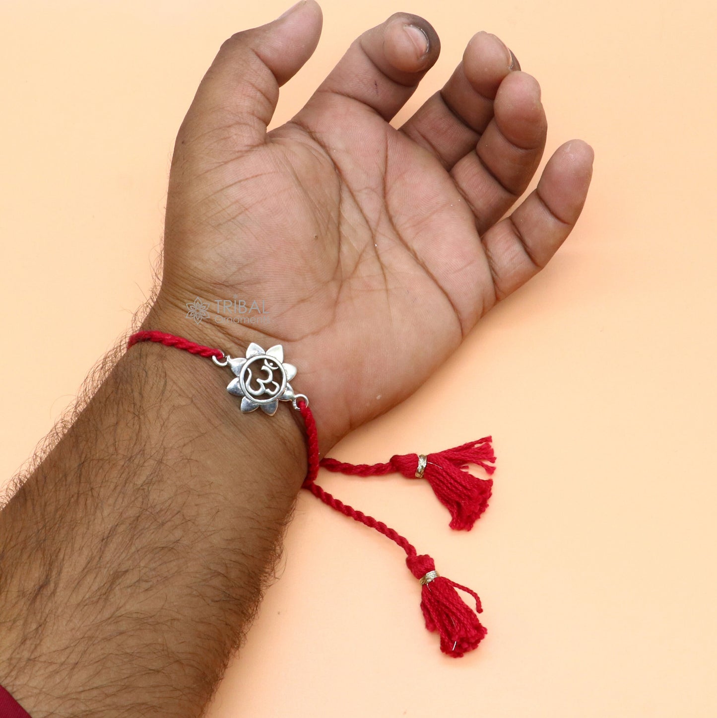 Sterling silver "AUM OM" mantra thread rakhi bracelet with red thread from TRIBAL ORNAMENTS, featuring intricate silver detailing.