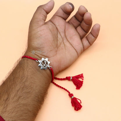 Sterling silver "AUM OM" mantra thread rakhi bracelet with red thread from TRIBAL ORNAMENTS, featuring intricate silver detailing.