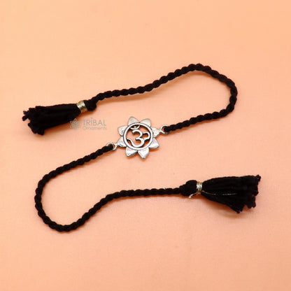 Sterling silver "AUM OM" mantra thread rakhi bracelet with red thread from TRIBAL ORNAMENTS, featuring intricate silver detailing.