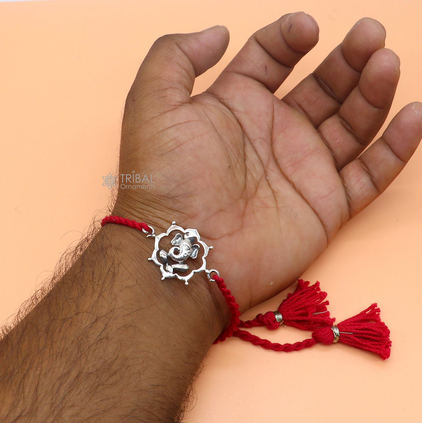 Sterling silver Lord Ganesha pendant on red thread rakhi bracelet by TRIBAL ORNAMENTS, featuring intricate Ganesha design.