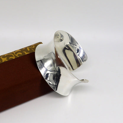 Sterling silver cuff bracelet with a unique curved design, bright shiny finish, elegant Bollywood-inspired style.