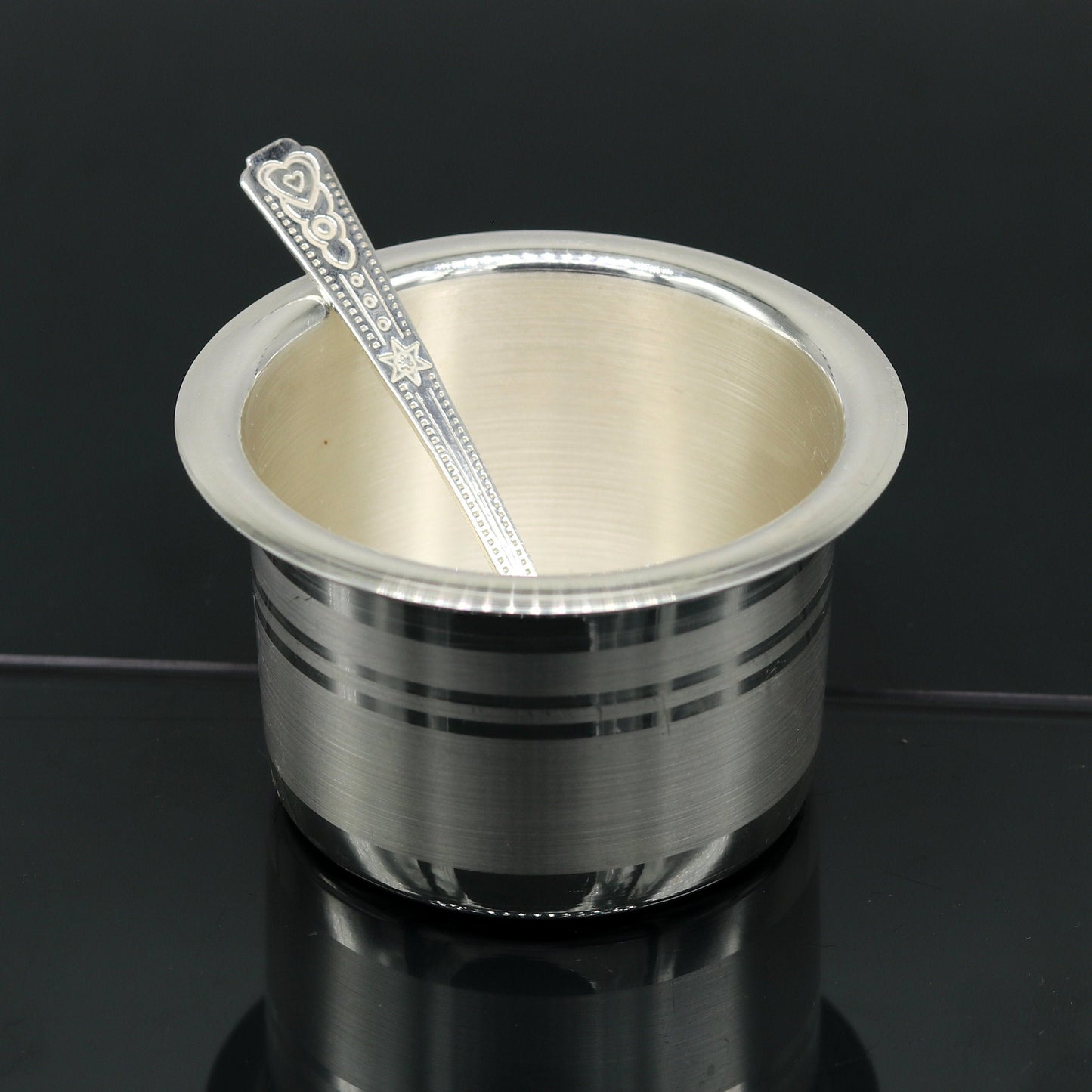 Handmade 999 pure silver baby feeding set with bowl and spoon by TRIBAL ORNAMENTS, featuring traditional silver vessels and utensils.