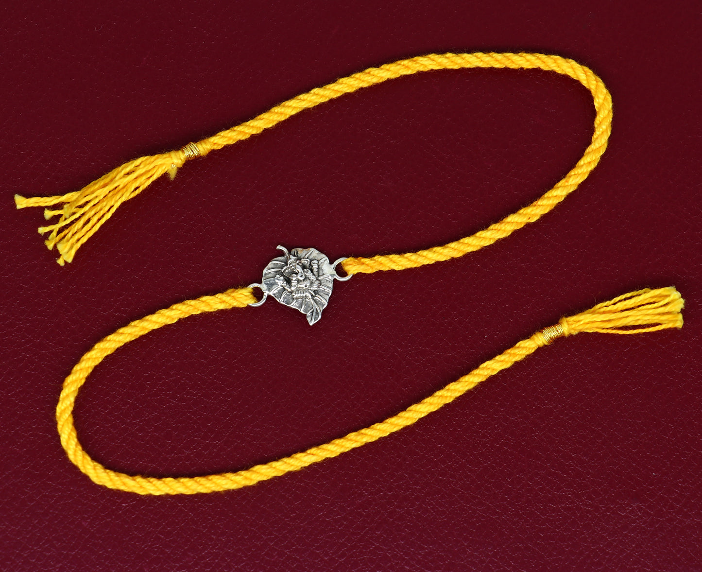 Sterling silver Ganesha design bracelet with yellow thread Rakhi from TRIBAL ORNAMENTS, featuring intricate silver craftsmanship.