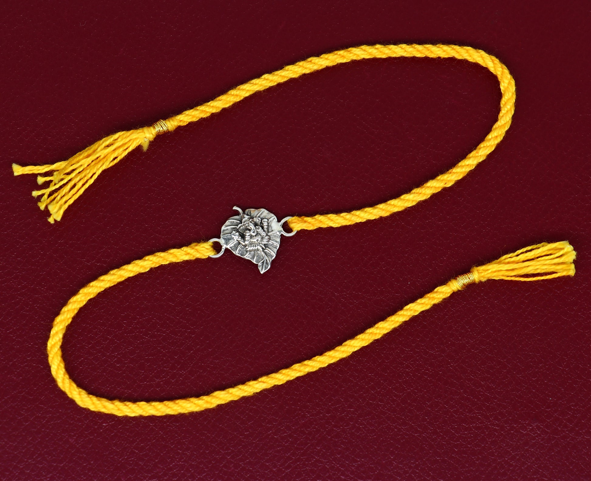 Sterling silver Ganesha design bracelet with yellow thread Rakhi from TRIBAL ORNAMENTS, featuring intricate silver craftsmanship.