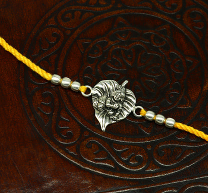 Sterling silver Krishna design bracelet with yellow thread rakhi, featuring Lord Krishna and Laddu Gopal motifs, by Tribal Ornaments.