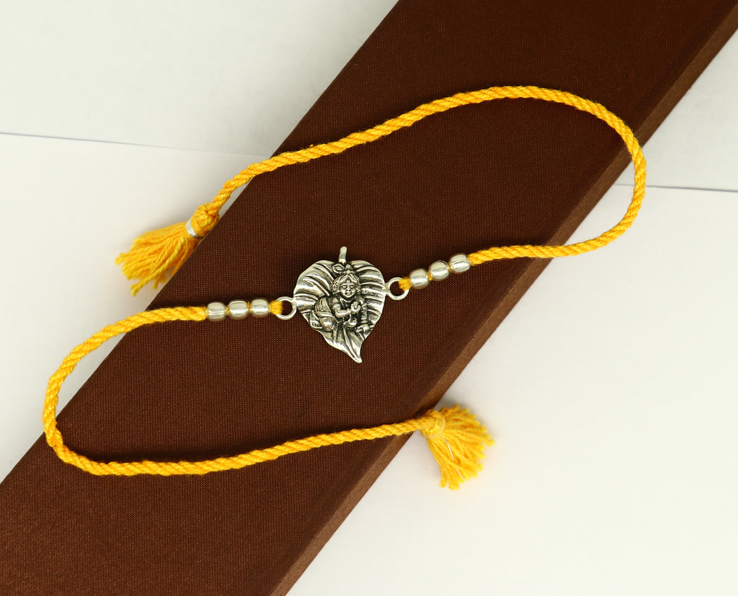 925 sterling silver Krishna design bracelet with yellow thread rakhi, featuring Lord Krishna motif from TRIBAL ORNAMENTS.