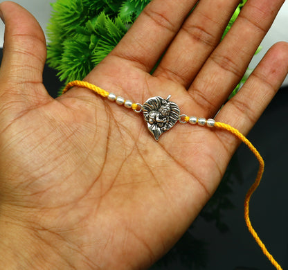Sterling silver Krishna design Rakhi bracelet with yellow thread, featuring Lord Krishna and Laddu Gopal motifs, by TRIBAL ORNAMENTS.