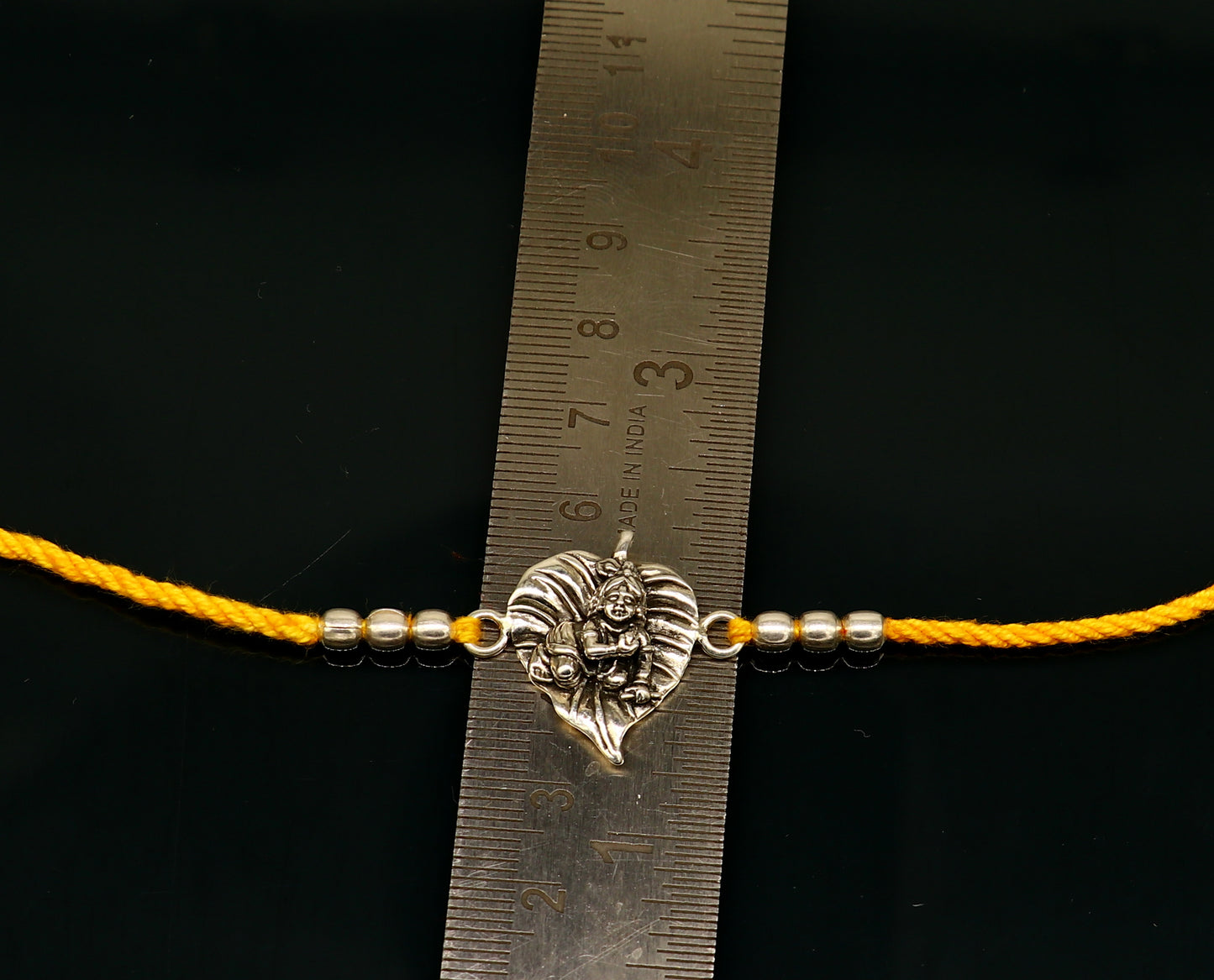 Sterling silver Krishna bracelet with yellow thread rakhi for religious occasions, featuring intricate Lord Krishna design.