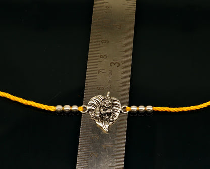 Sterling silver Krishna bracelet with yellow thread rakhi for religious occasions, featuring intricate Lord Krishna design.