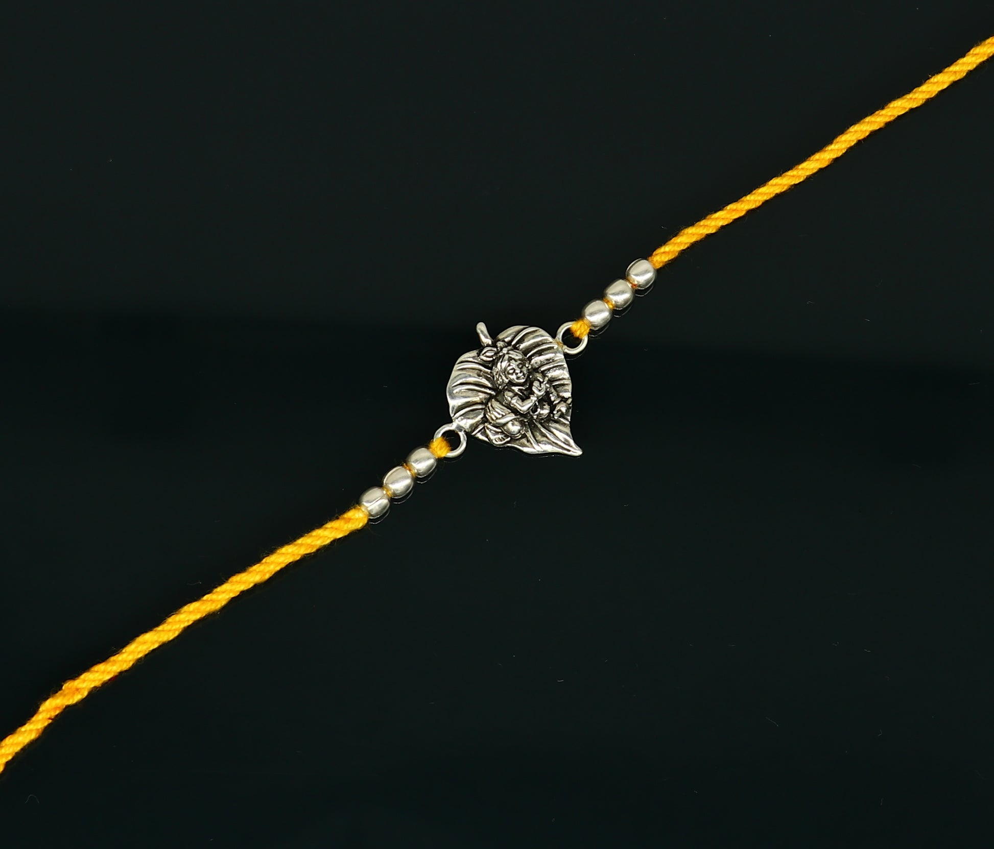 Sterling silver Krishna design bracelet with yellow thread rakhi, featuring Lord Krishna's image, from TRIBAL ORNAMENTS.