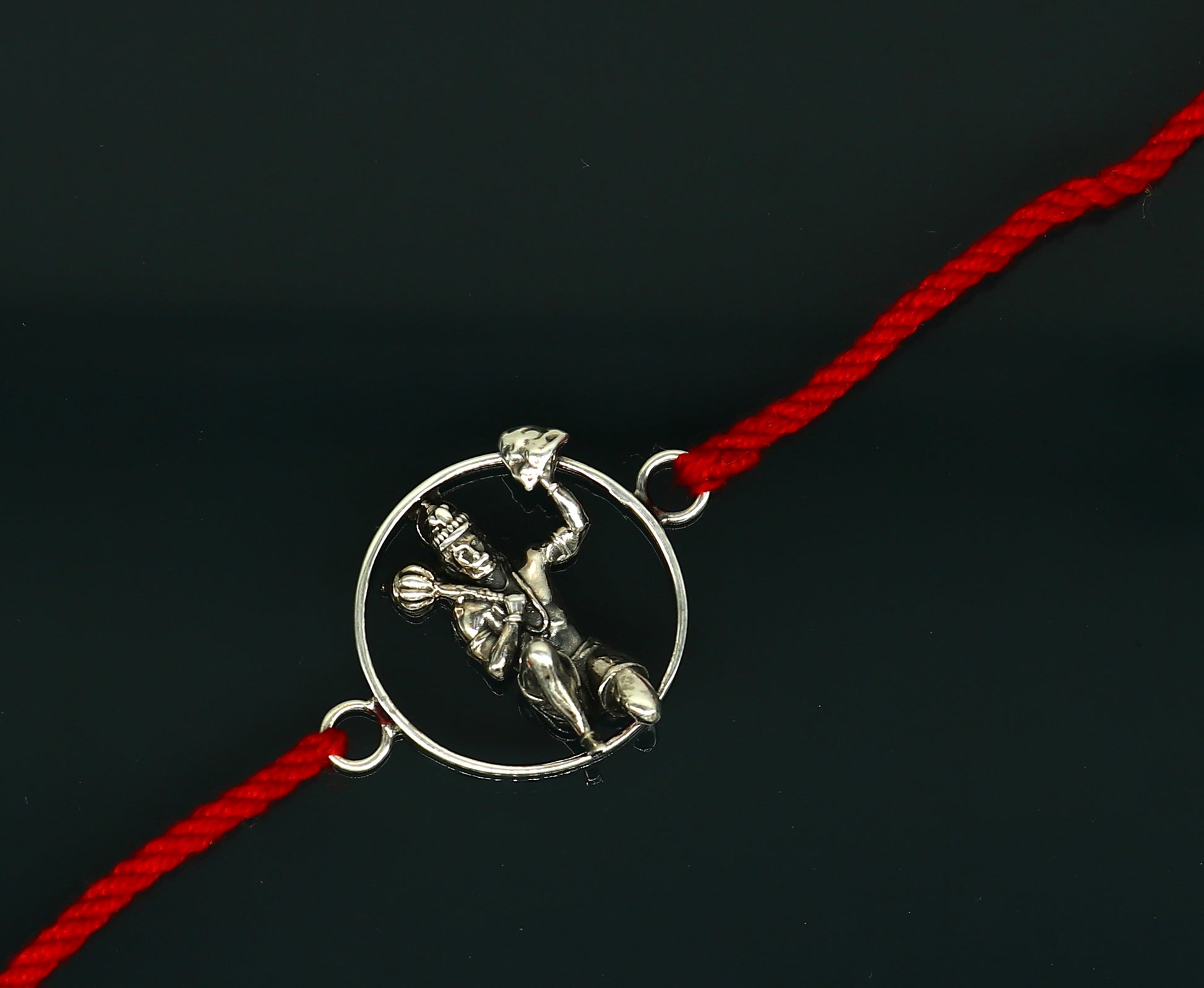 Sterling silver Hanuman idol bracelet with red thread rakhi, featuring intricate tribal ornament design.