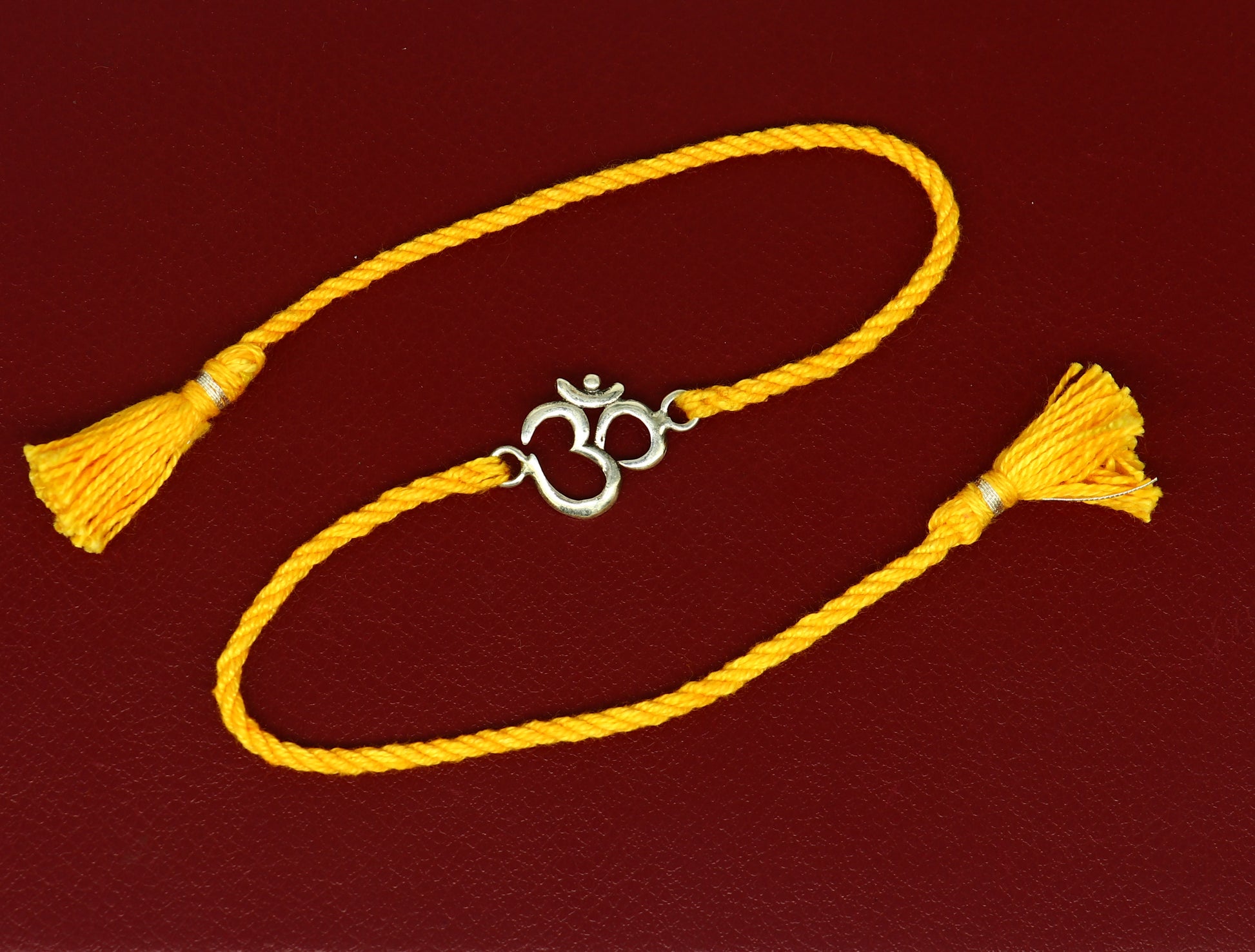 925 silver OM design bracelet with yellow thread rakhi, featuring custom sterling silver craftsmanship and intricate Aum motif.