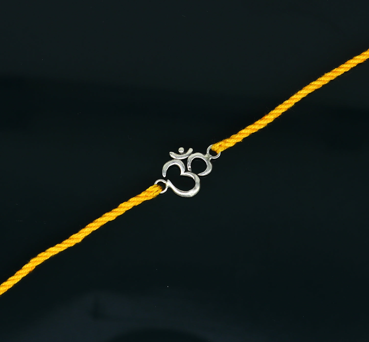 925 sterling silver OM design rakhi bracelet with yellow thread from Tribal Ornaments, featuring intricate silver craftsmanship and vibrant thread.