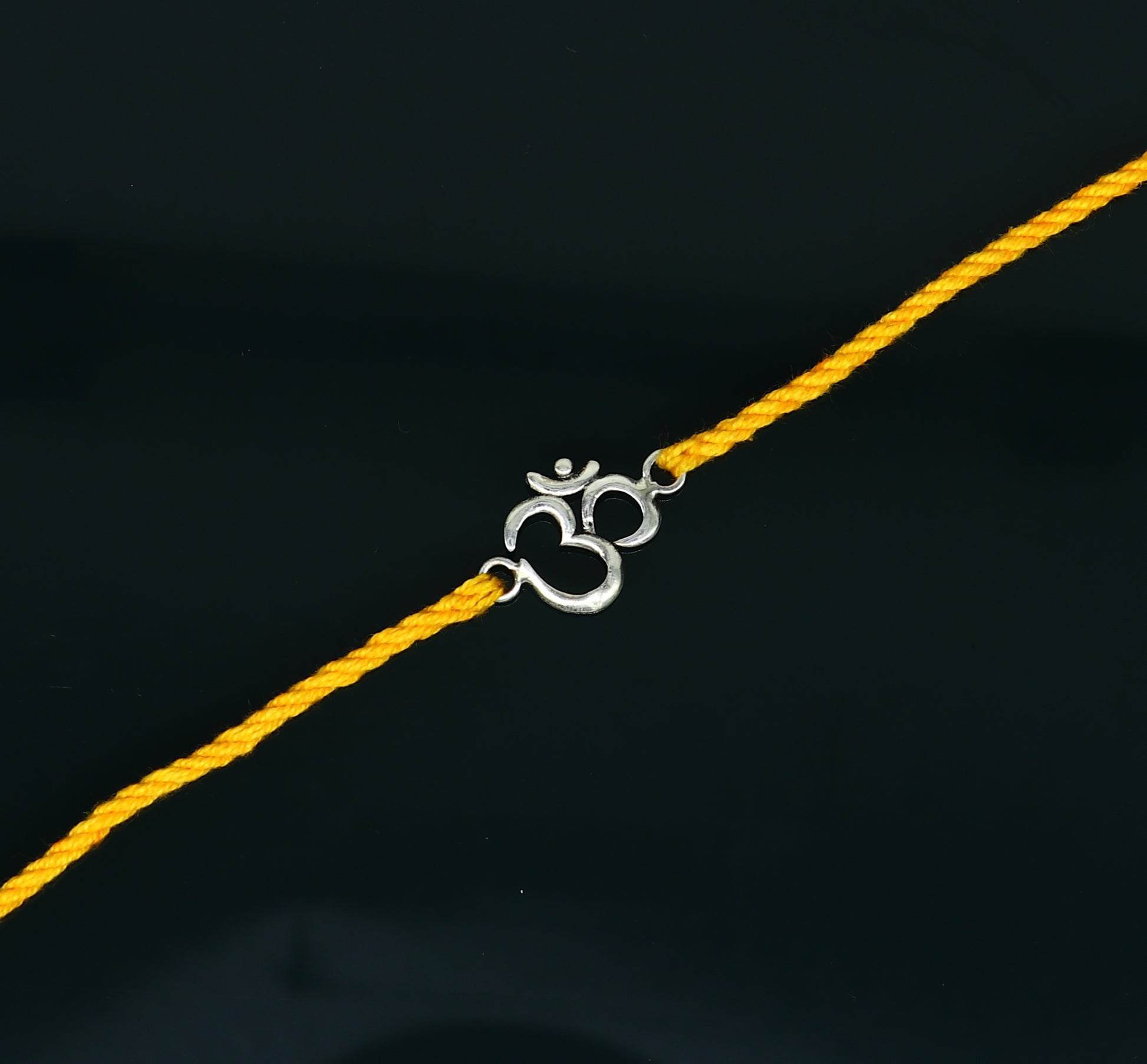 925 sterling silver OM design rakhi bracelet with yellow thread from Tribal Ornaments, featuring intricate silver craftsmanship and vibrant thread.