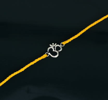 925 sterling silver OM design rakhi bracelet with yellow thread from Tribal Ornaments, featuring intricate silver craftsmanship and vibrant thread.
