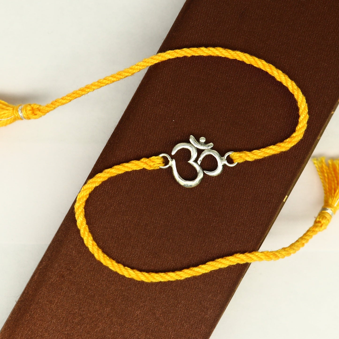 925 sterling silver OM design bracelet with vibrant yellow thread, custom rakhi by TRIBAL ORNAMENTS featuring intricate silver and red accents.